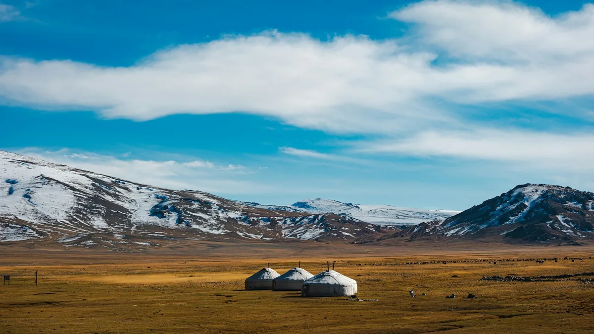 Traditional gers on the open Mongolian steppe beneath distant mountains