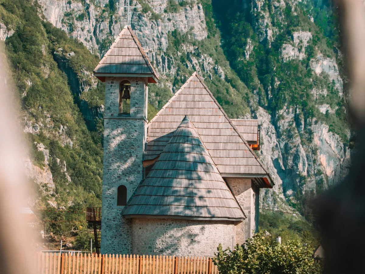 A stone chapel with a wooden bell tower set against the cliffs above Theth, Albania