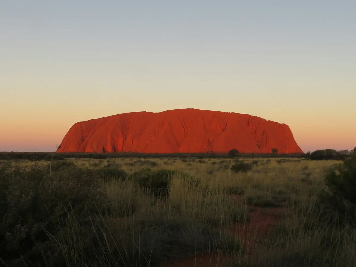 Uluru glowing red in the desert at sunset