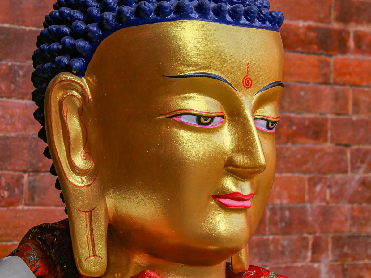 A golden Buddha statue with ornate red and white robes at a temple in Kathmandu, Nepal