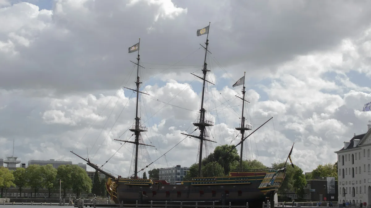 A replica 17th-century wooden sailing ship docked at a harbor