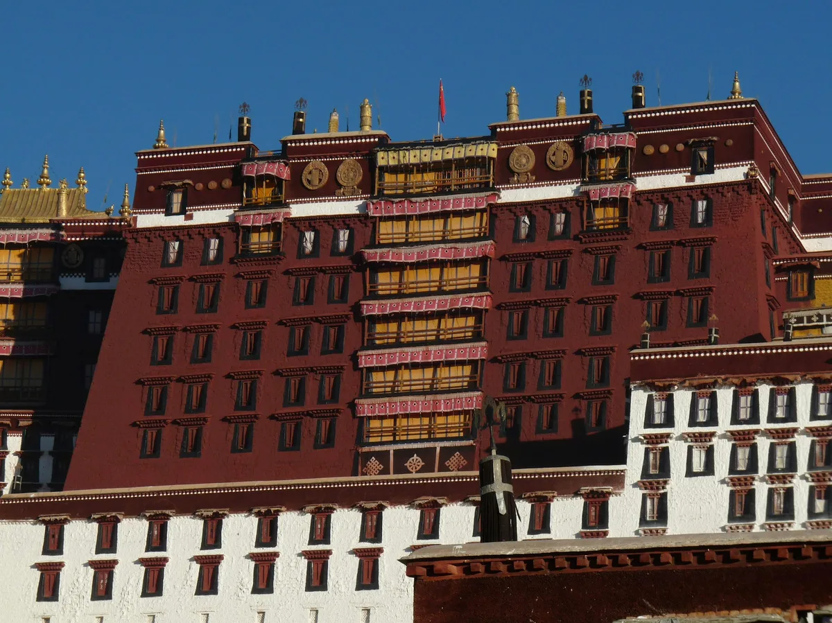 A large red Tibetan building beneath a mountain backdrop near Lhasa