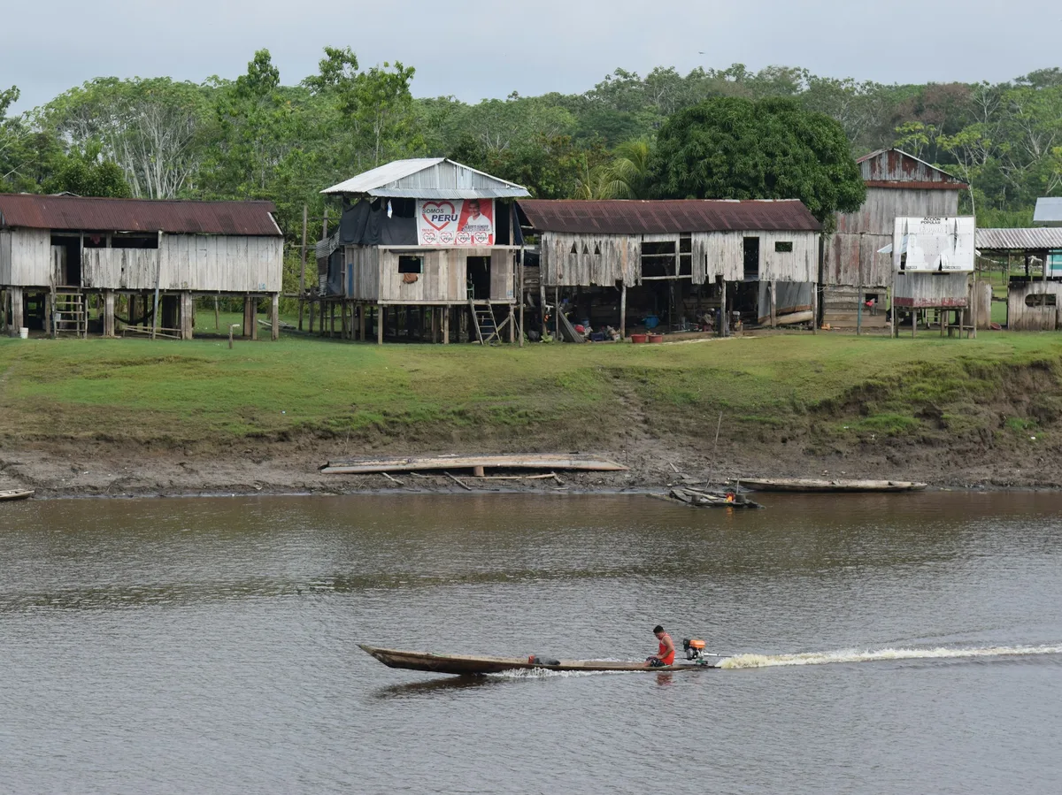 A small boat navigating past a fishing village built on stilts over a coastal lagoon