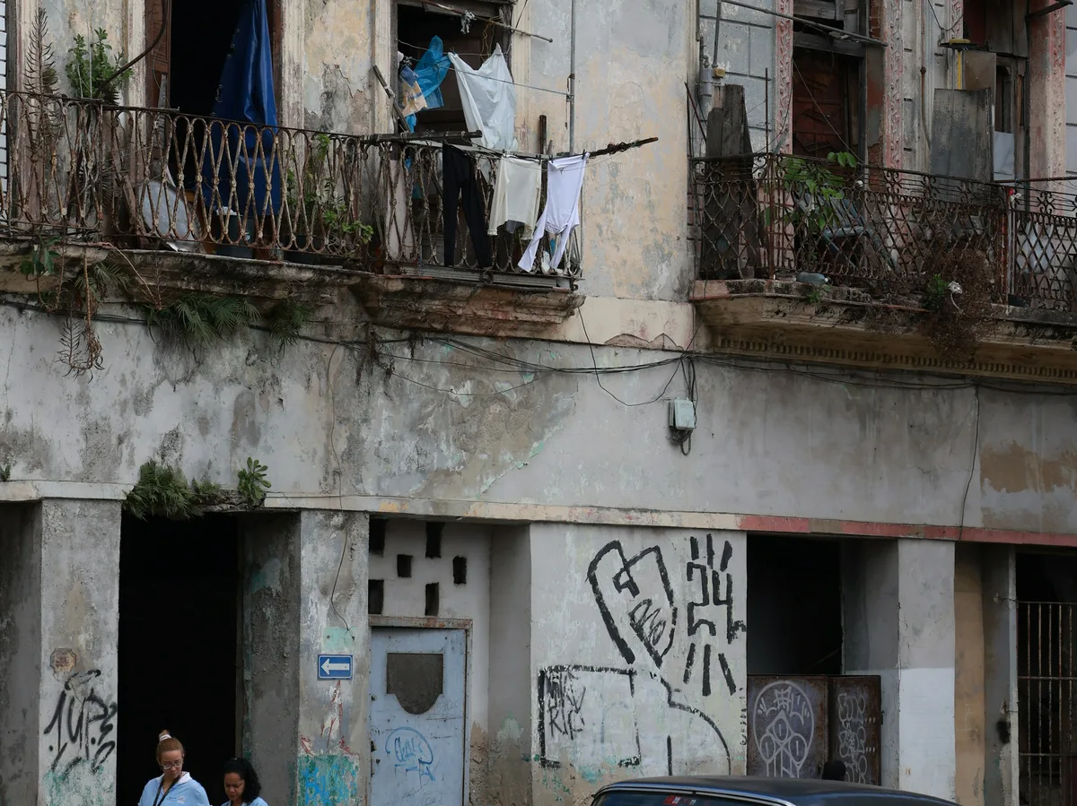A weathered Havana apartment building with wrought-iron balconies, laundry hanging out to dry, and street-level graffiti