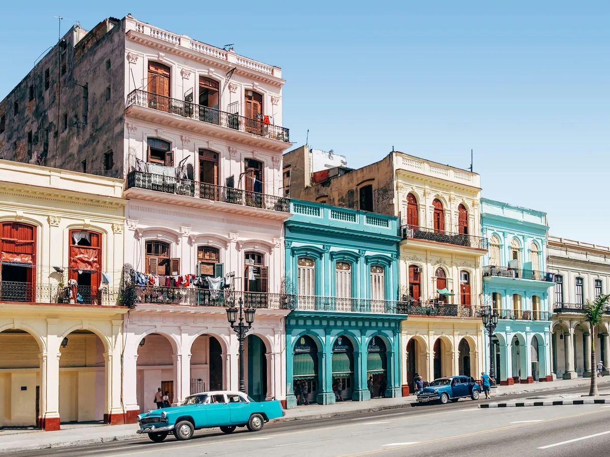 Vintage American cars parked outside colourful colonial buildings on a street in Old Havana, Cuba