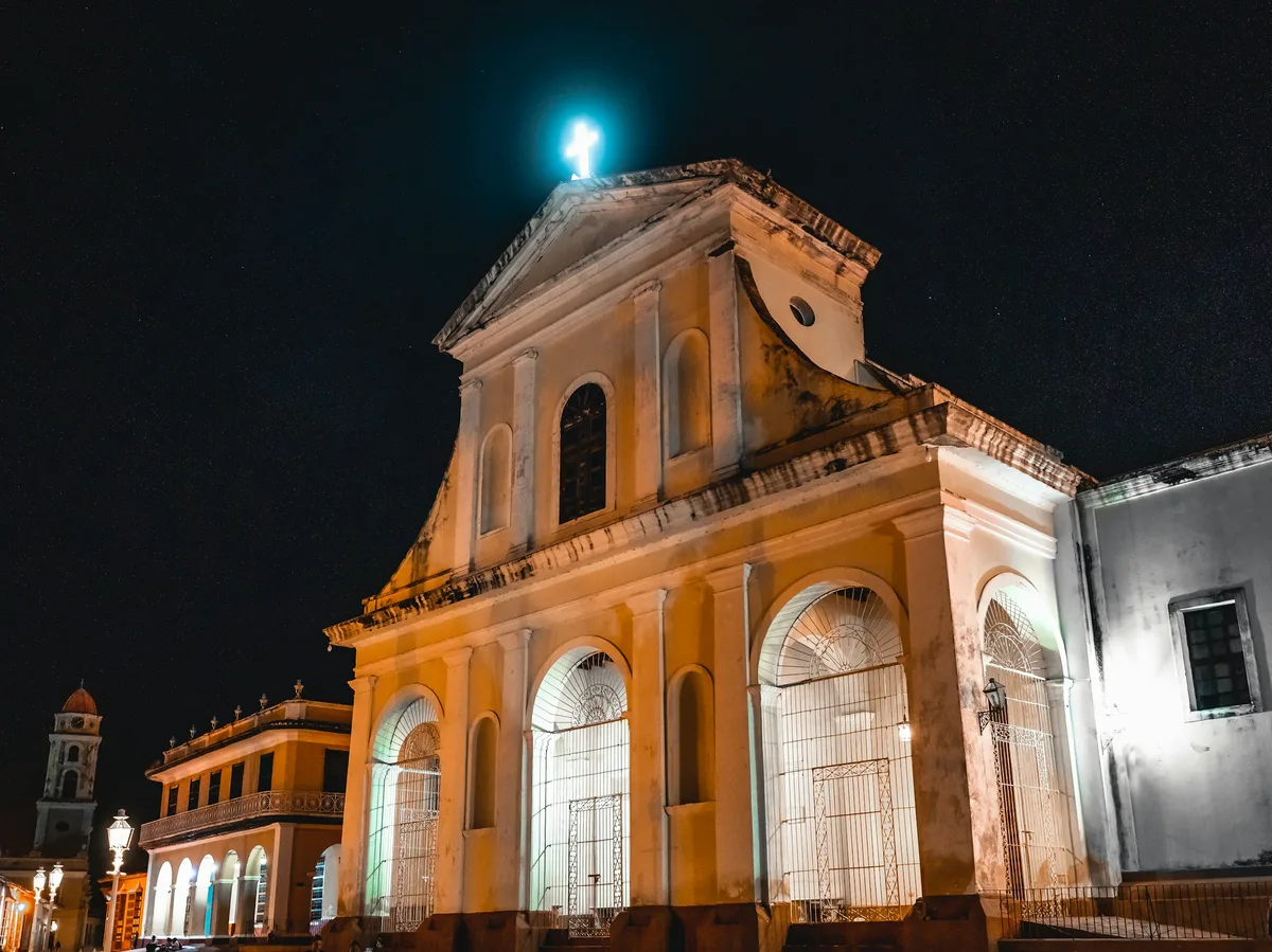The illuminated facade of Trinidad's parish church at night, with the city's colonial bell tower visible alongside