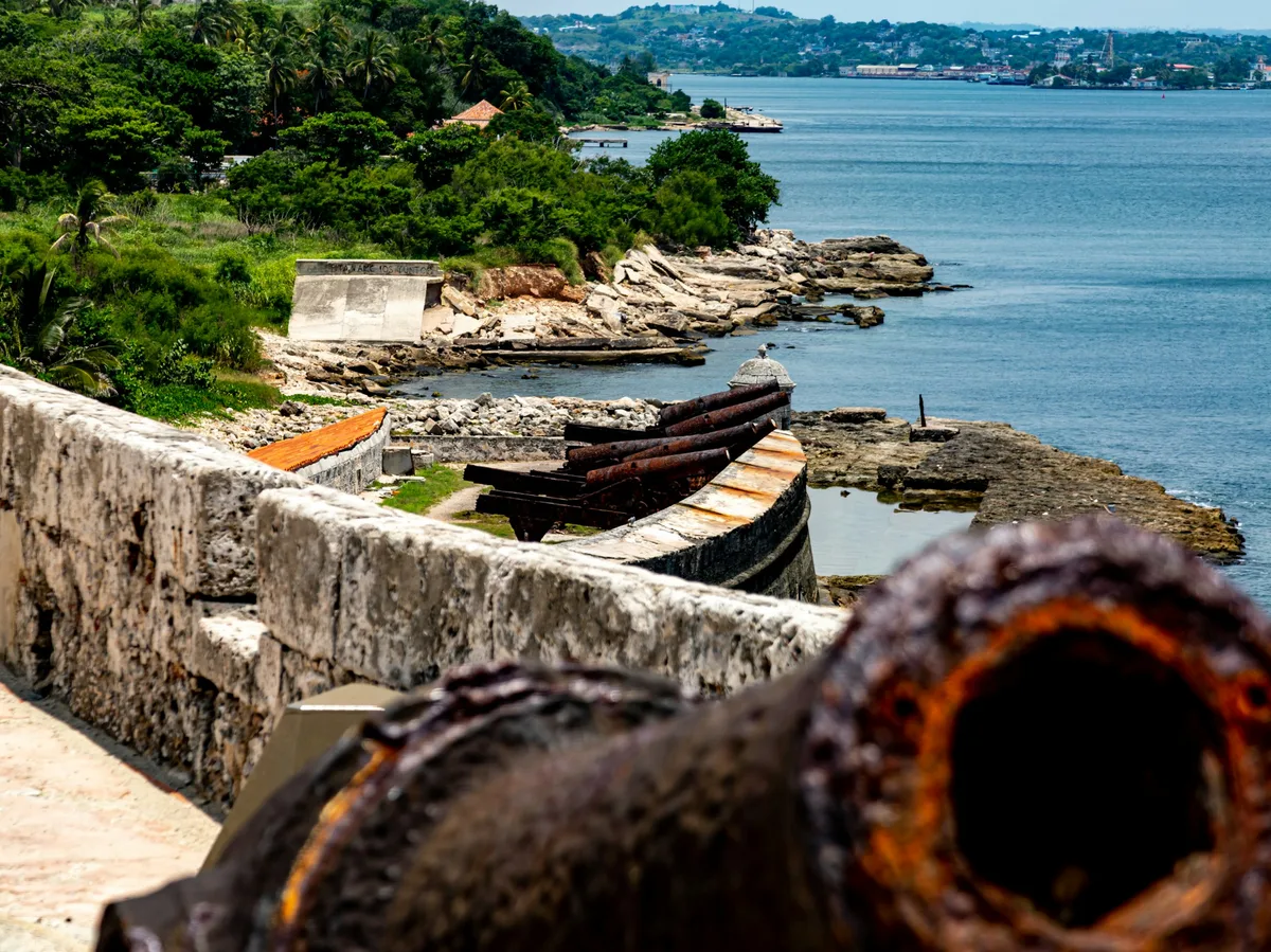 Old cannons on the stone ramparts of a colonial fortress overlooking a bay in Cuba