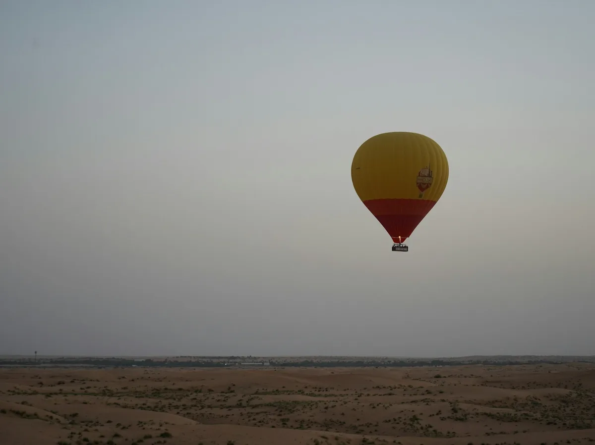 A hot air balloon floating over the Dubai desert at dawn