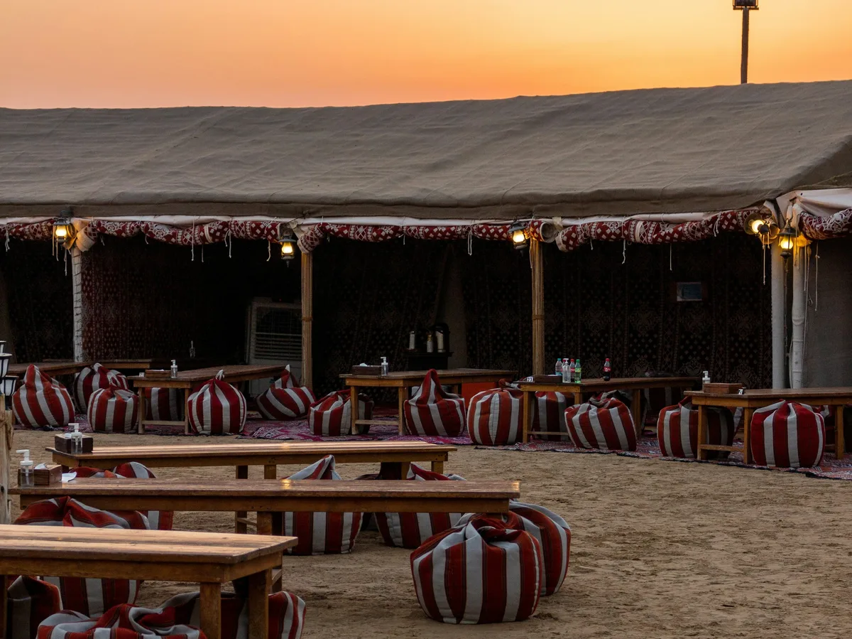 A desert camp dining setup with string lights at dusk near Dubai
