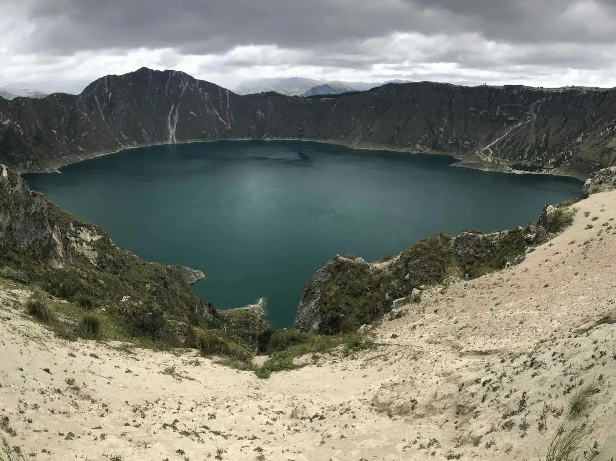 A turquoise volcanic crater lake surrounded by green Andean mountains in Ecuador