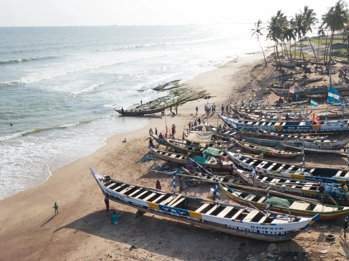 Traditional wooden fishing boats pulled up on a sandy beach on Ghana's western coast