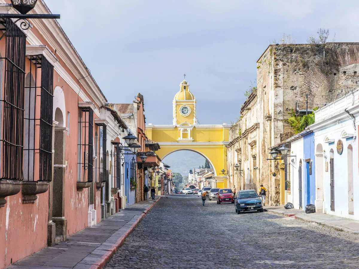 A cobblestone street in Antigua, Guatemala, lined with colonial buildings and a distant volcano