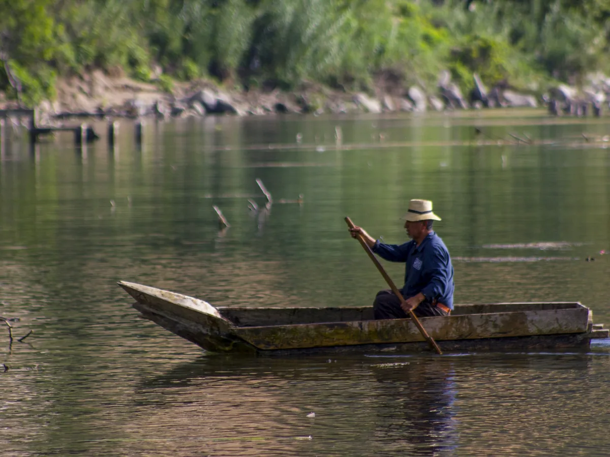 A traditional wooden boat on the Rio Dulce river in Guatemala, framed by lush riverbank forest