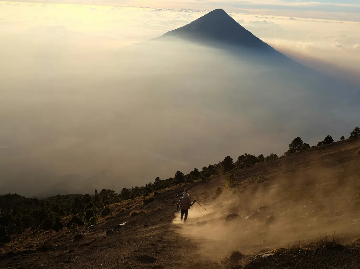 A hiker walking a highland trail toward misty mountains in rural Guatemala