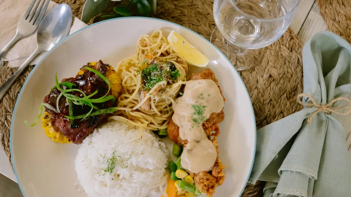 A plate of rice, grilled meats, and pasta at a restaurant table