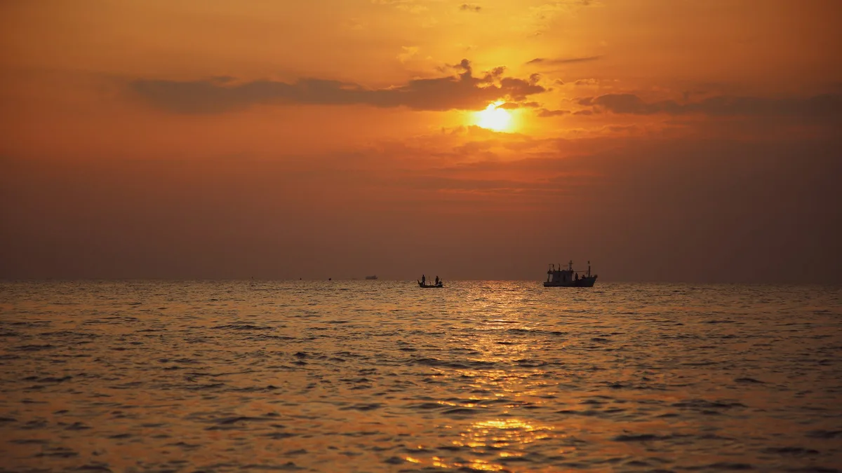 A boat silhouetted against a colorful sunset over the ocean