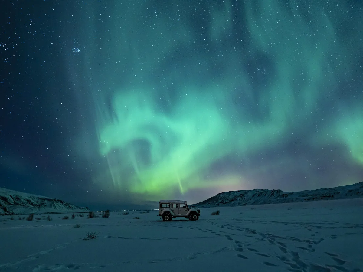 Green aurora borealis lighting up the night sky over a snow-covered Icelandic field