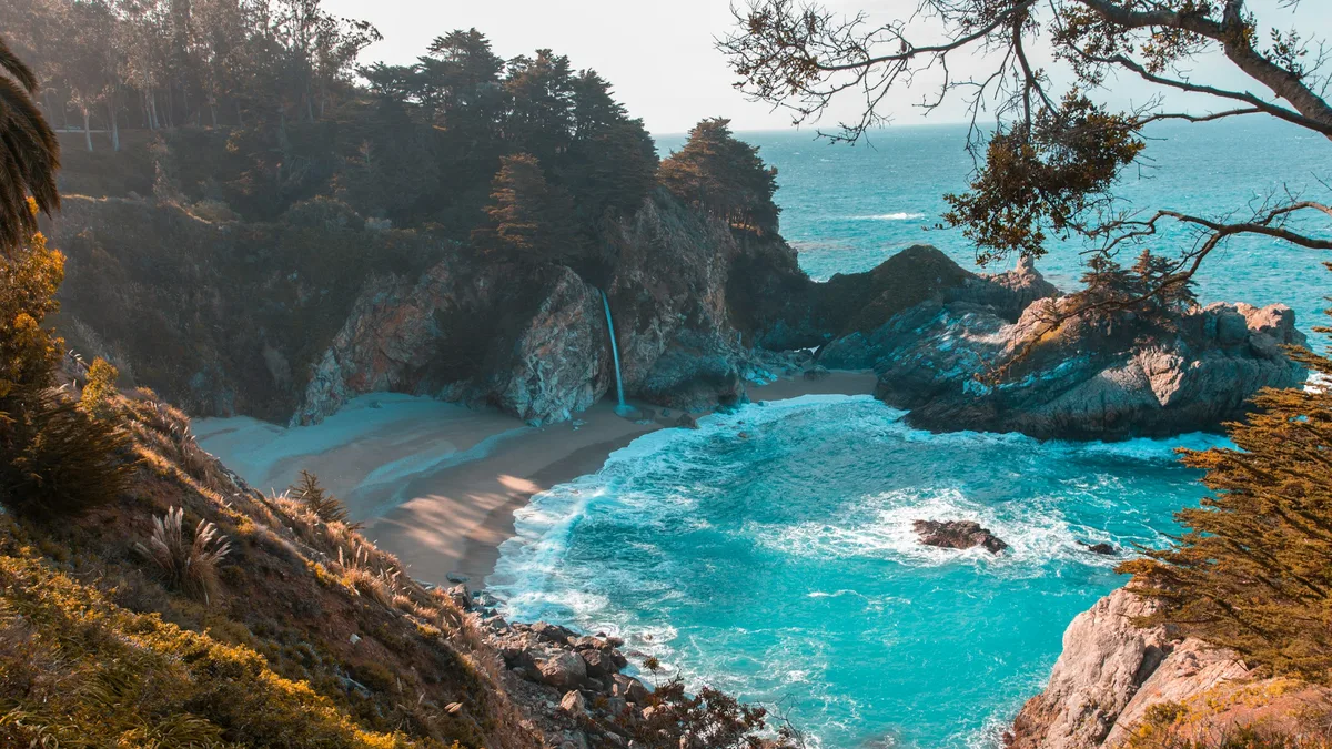 A waterfall cascading onto a secluded beach along a rugged coastline