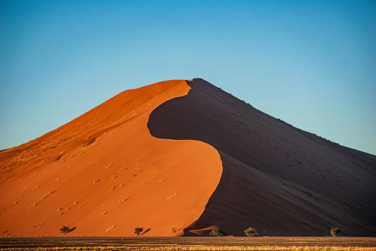 Orange sand dunes of the Namib Desert under a blue sky in Namibia