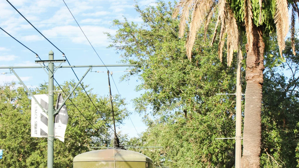 A classic green streetcar traveling down a tree-lined avenue