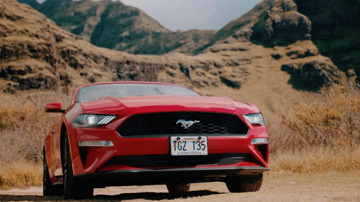 A red Ford Mustang convertible with a Hawaii license plate parked against a dramatic mountain backdrop