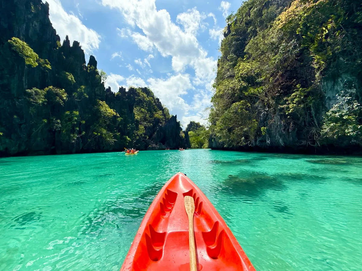 Kayaking through turquoise water beneath limestone cliffs at El Nido, Palawan, Philippines