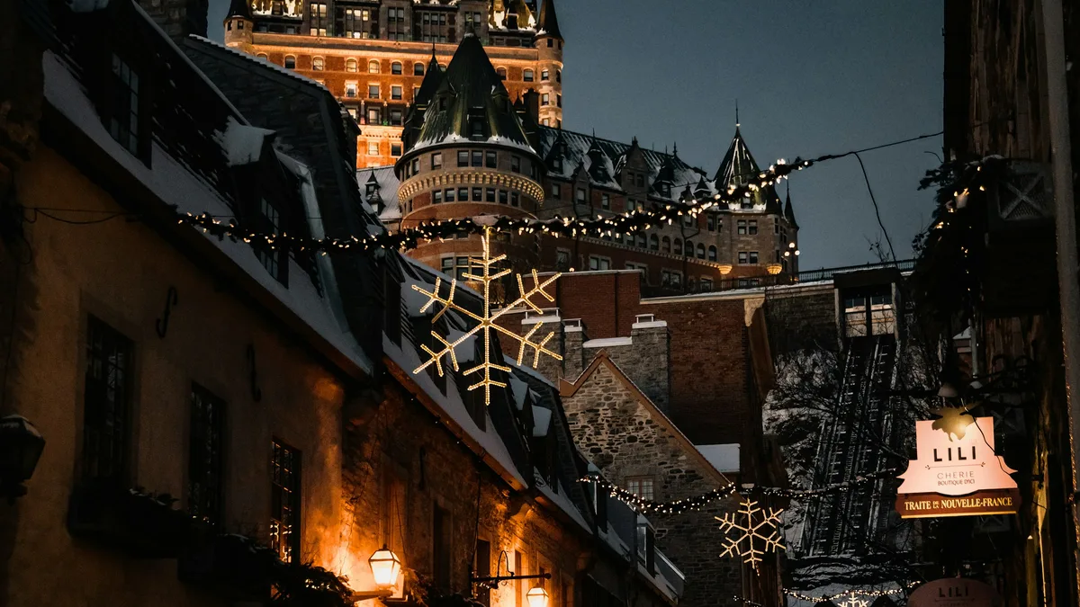 A snowy street lined with historic stone buildings below the Chateau Frontenac in Old Quebec at night, strung with holiday lights