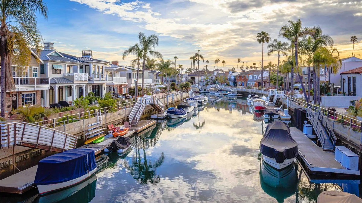 Boats moored along a calm residential canal lined with palm trees and waterfront homes