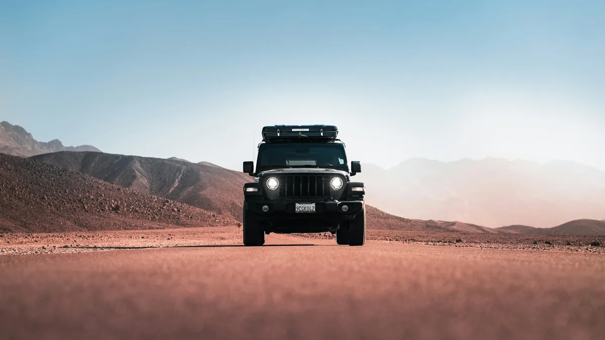 A Jeep off-road vehicle on a desert road with rugged mountains in the background