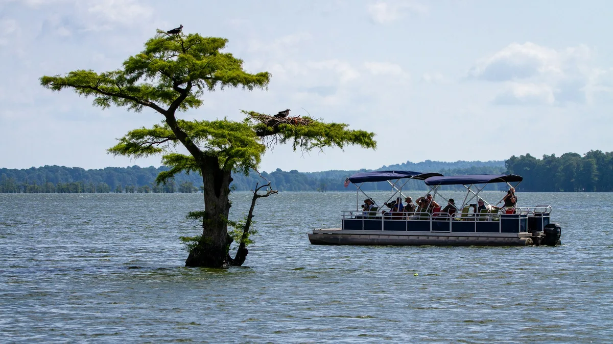 A pontoon tour boat carrying passengers across calm water on a sunny day