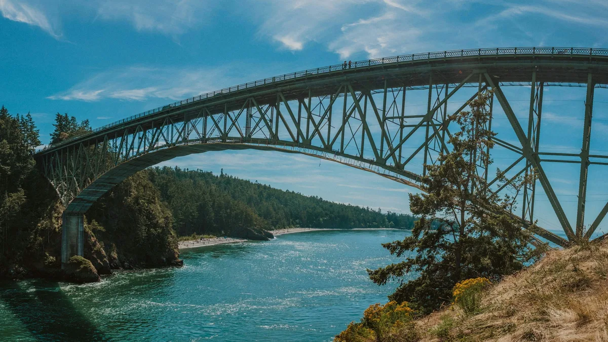A tall bridge spanning a narrow channel between forested cliffs