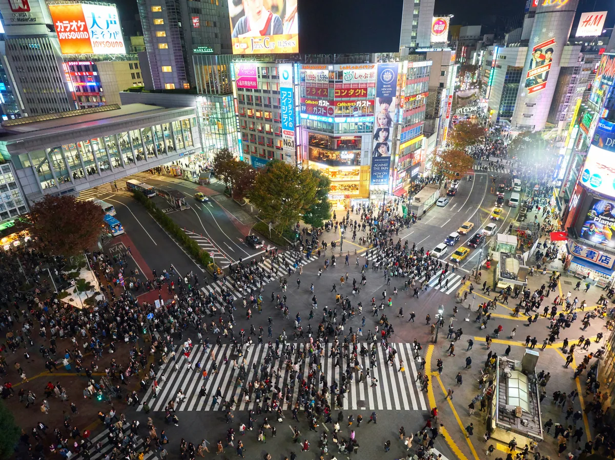 Crowds of people crossing the neon-lit Shibuya Scramble intersection at night in Tokyo, Japan