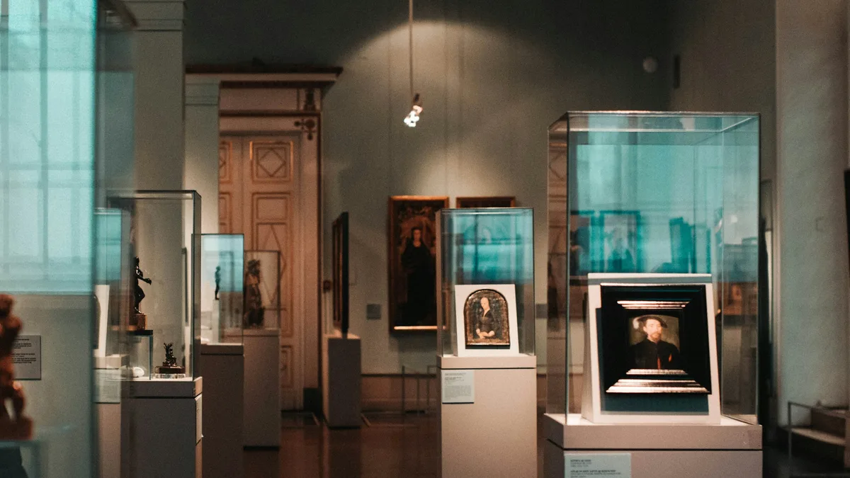Glass display cases with framed paintings and artifacts inside a museum gallery