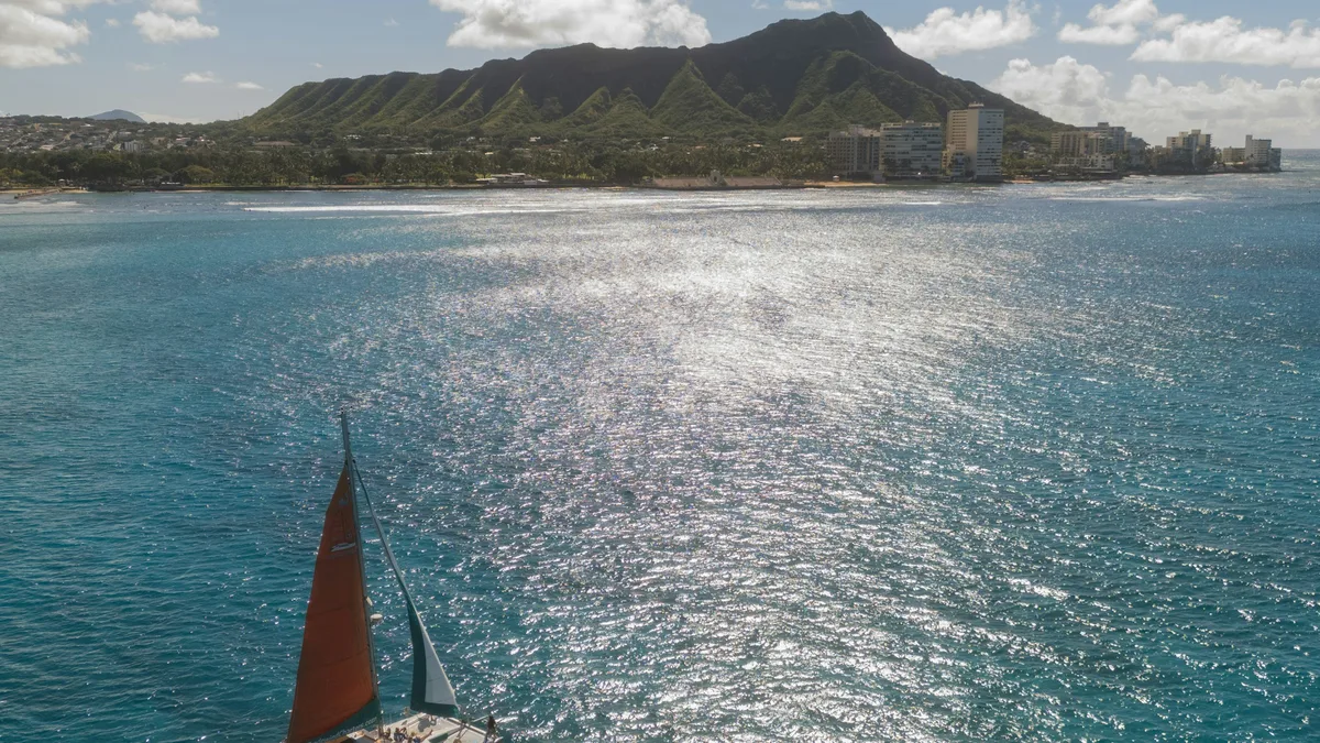A sailboat's red and white sails on the water near Diamond Head in Waikiki, Honolulu